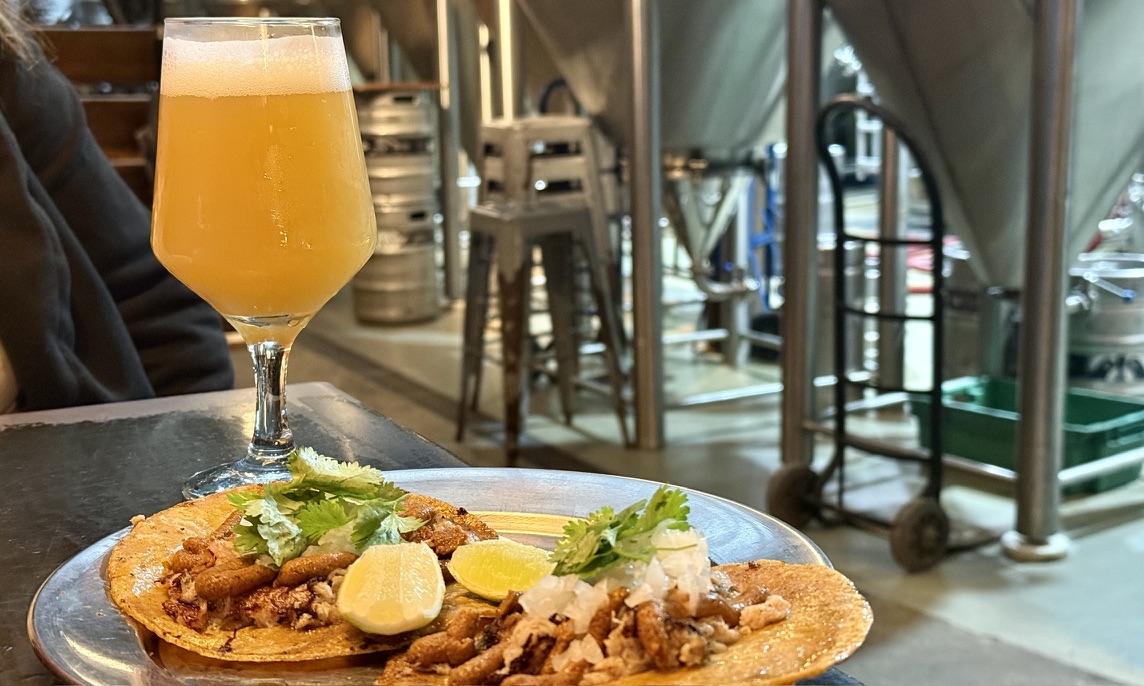 A hazy craft beer with fresh tacos beside brewery tanks